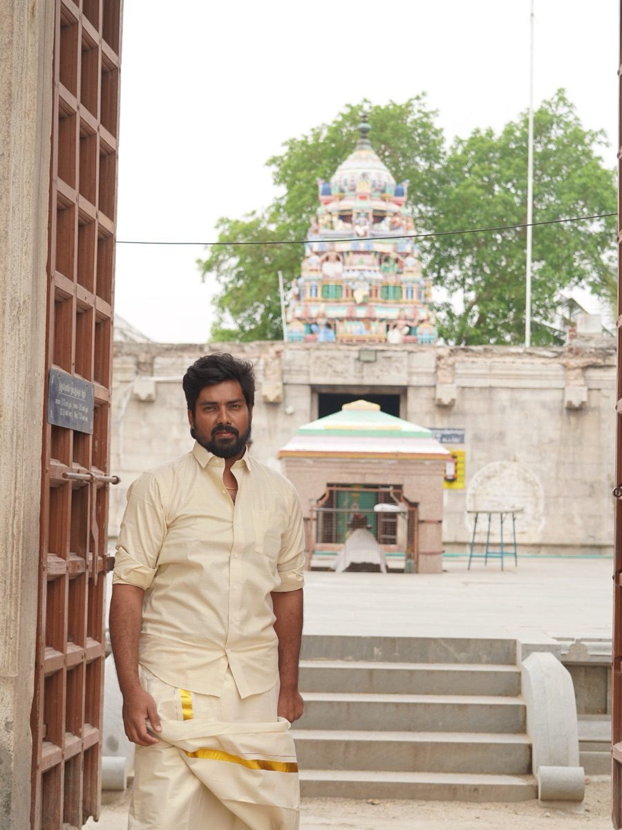 Avinash Srinivasan, இந்த கட்டுரையை எழுதியவர், ஒரு தமிழ் கோயில் வாசலில் வேட்டி சட்டையுடன் நிற்கிறார்.